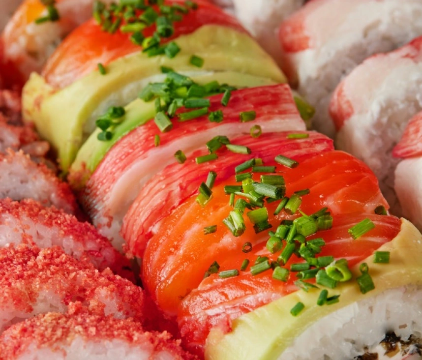 A variety of freshly made sushi rolls with imitation crab, avocado, and salmon on top.