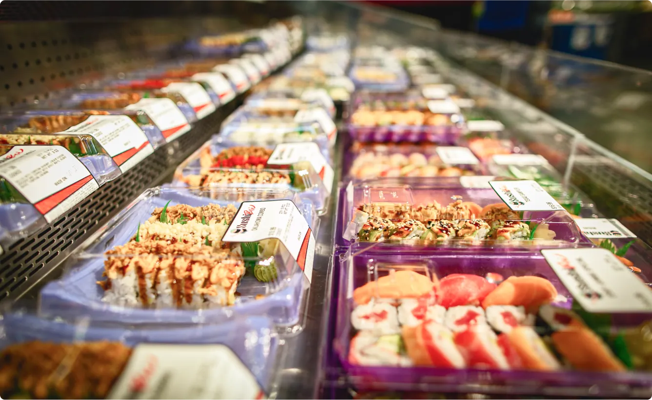 Eye-level shot of a variety of sushi rolls and other sushi products in the shelves of a grocery store.