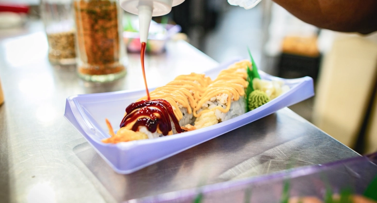 Person adding various sauces to their grab-and-go sushi roll from Sushiboi.