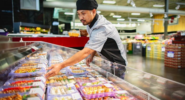 Sushi chef in a grocery store laying out a display of freshly prepared sushi.
